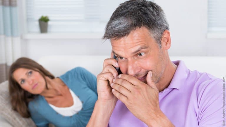 Eifersucht und Selbstwert. Mann und Frau. Er telefoniert heimlich, sie schaut skeptisch.