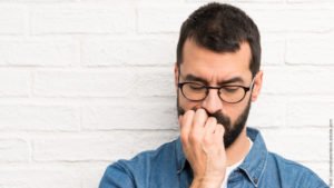 Unsicherheit überwinden beim Flirten. Mann schaut nach unten und stützt das Gesicht in seine Hand.