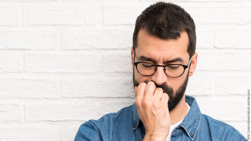 Unsicherheit überwinden beim Flirten. Mann schaut nach unten und stützt das Gesicht in seine Hand.