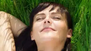 Was passiert in Hypnose? Frau liegt mit geschlossenen Augen und entspannt auf einer Wiese.