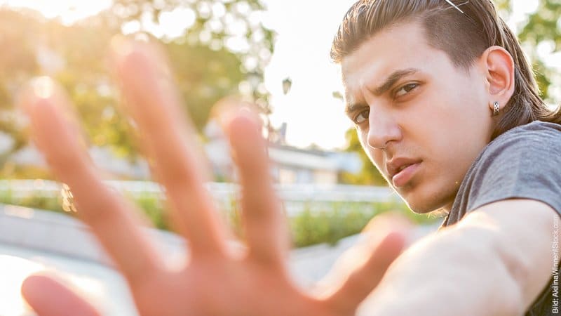 Angst vor Nähe – reicht mehr Mühe geben? Junger Mann schaut nach hintern und wart mit der Hand ab.