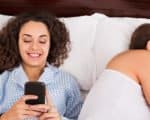 Einmal Sex to go - Emanzipation geht im Internet fremd. Mann und Frau im Bett. Er schläft, sie lacht ins Handy.