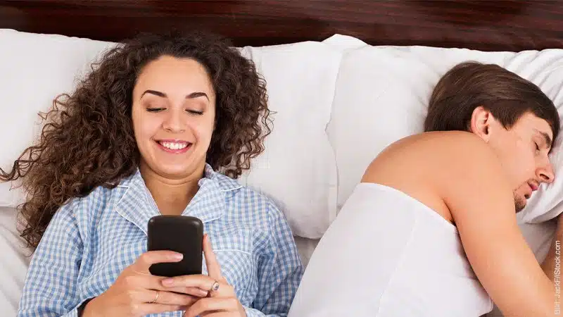 Einmal Sex to go - Emanzipation geht im Internet fremd. Mann und Frau im Bett. Er schläft, sie lacht ins Handy.