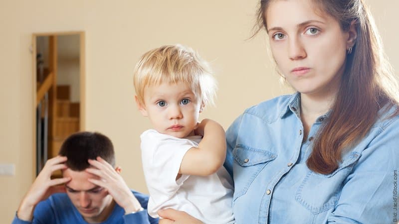 Trennung als Eltern - Wenn das Elternsein die Beziehung überlagert. Traurig schauende Frau trägt Kleinkind auf dem Arm, der Mann stütz den Kopf in die Hände.