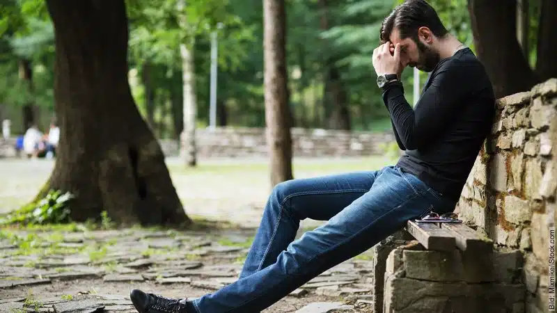 Krise im Urlaub: Überlebt das deine Beziehung? Mann sitzt verzweifelt auf einer Mauer.