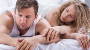 Manipulation statt Empathie. Mann und Frau im Bett. Die Frau versucht die Aufmerksamkeit ihres Mannes zu bekommen, hat ihre Hand auf seinem Arm. Er schaut unbeteiligt auf die Seite.