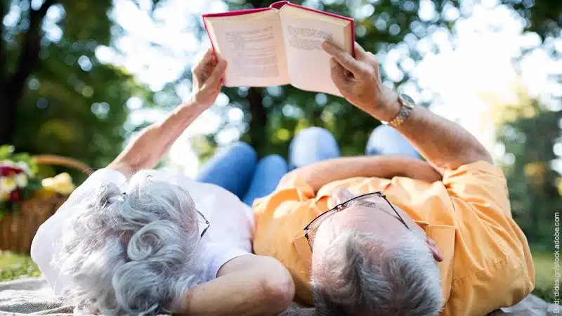Nähe in Beziehungen - der Nähe Pol. Ein älteres Paar liest in einem Garten gemeinsam in einem Buch.