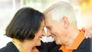 Die Sprachen der Liebe. Ein älteres Paar schaut sich liebevoll an, dabei berühren sie sich Stirn an Stirn.