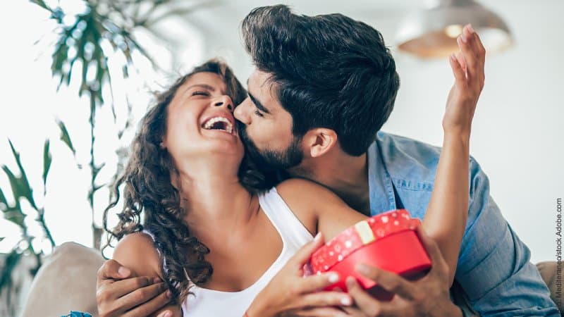 Valentinstag - leider doch nicht doof. Ein Paar freut sich, er küsst sie. Sie hält ein Geschenk in ihren Händen.