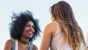 Beziehung verbessern durch 7 Power-Fragen. Zwei Frauen unterhalten sich angeregt, die eine hat lange blonde Haare und ist von hintern zu sehen, die andere hat schwarze Locken, lacht und ist von vorn zu sehen.