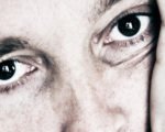 Emotionale Abhängigkeit – needy sein. Mann mit großen braunen Augen schaut bedürftig. Er hat den Kopf in die Hand gestützt.