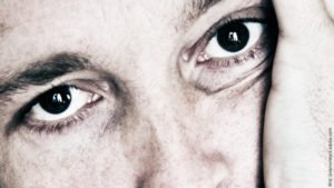Emotionale Abhängigkeit – needy sein. Mann mit großen braunen Augen schaut bedürftig. Er hat den Kopf in die Hand gestützt.