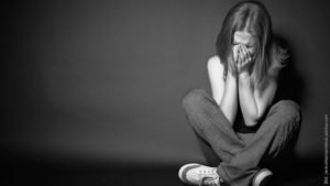 Betrogen worden - 8 Phasen und 11 Tipps. Frau sitzt auf dem Boden und hält ihre Hände vor ihr Gesicht. Sie sieht traurig aus. Schwarz-weiß Foto.