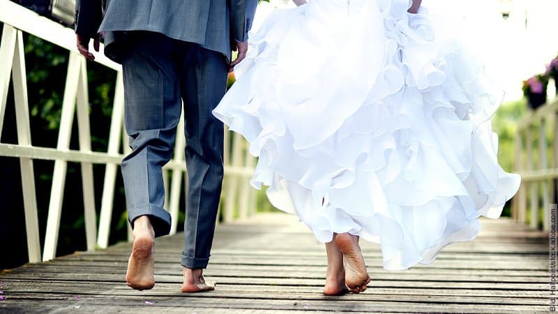 Die perfekte Hochzeit. Hochzeitspaar läuft barfuß auf einem Weg, der aus Planken besteht.