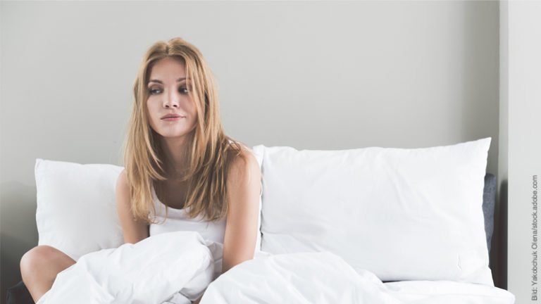 Nicht schlafen können ohne den Partner. Frau sitzt alleine im zerwühlten Bett.