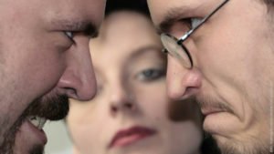 Gilt Eifersucht als Liebesbeweis? Zwei Männer schauen sich wütend an, Frau schaut unbeteiligt.