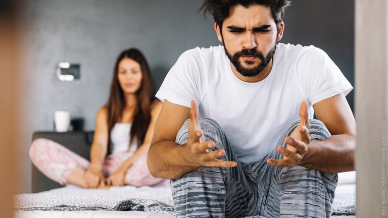 Hilflosigkeit, Wut und Ärger bei Streit in der Partnerschaft. Mann und Frau sitzen auf dem Bett, der Mann gestikuliert verzweifelt.