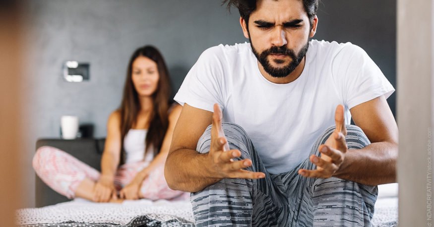 Hilflosigkeit, Wut und Ärger bei Streit in der Partnerschaft. Mann und Frau sitzen auf dem Bett, der Mann gestikuliert verzweifelt.