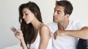 Eifersucht und Trennung. Mann schaut eifersüchtig zu seiner Frau, die in ihr Handy schaut. Beide sitzen auf dem Bett. Ob eine Trennung bevorsteht?