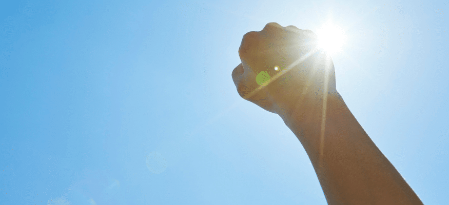 Hand ist zur Faust geballt in den blauen Himmerl gereckt. Die Sonne scheint. Du bist nicht kaputt – warum du nach einem Betrug stärker bist als je zuvor