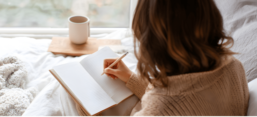 Bild: eine Frau von hinten, die in ein Notizbuch schreibt. Helle Farben. Mini-Journaling nach dem Betrug 3 Fragen, die dich raus aus der Opferrolle holen