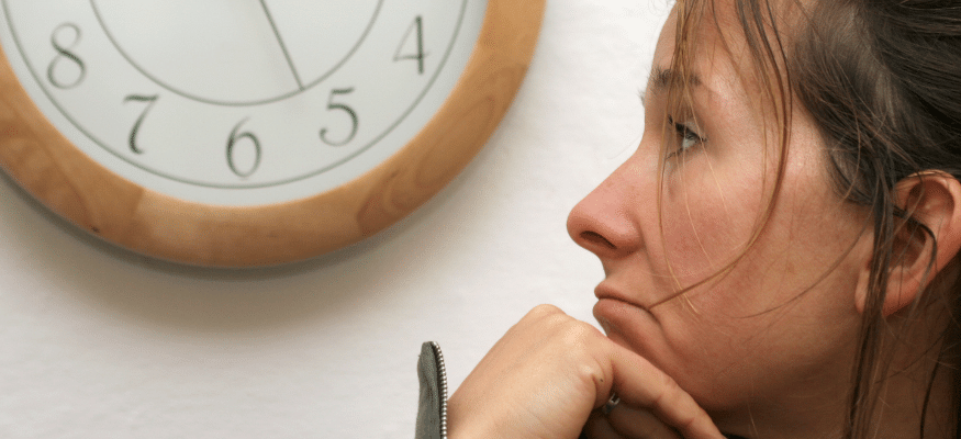 Frau wartet, stützt den Kopf auf die Hand und beobachtet eine Uhr an der Wand:wie lange dauert es, das Fremdgehen zu überwinden