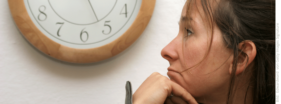 Frau wartet, stützt den Kopf auf die Hand und beobachtet eine Uhr an der Wand:wie lange dauert es, das Fremdgehen zu überwinden